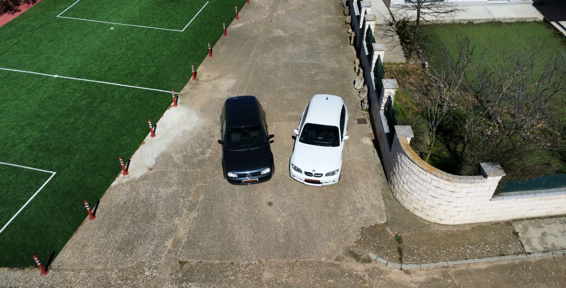 Un Golf IV negro y un BMW blanco vistos desde un dron, aparcados junto a un campo de fútbol